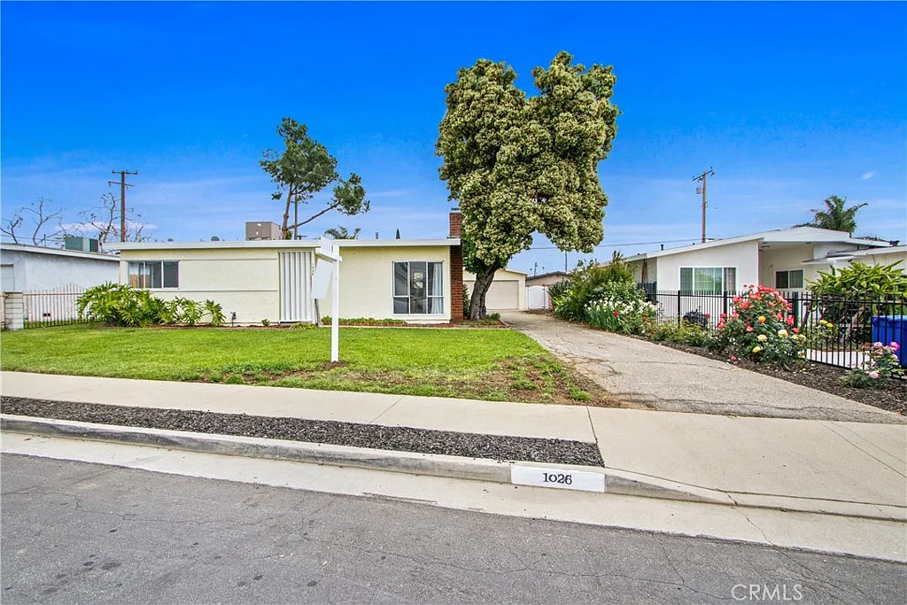 Single-story house real estate with light walls, lawn, tree, path, and greenery.