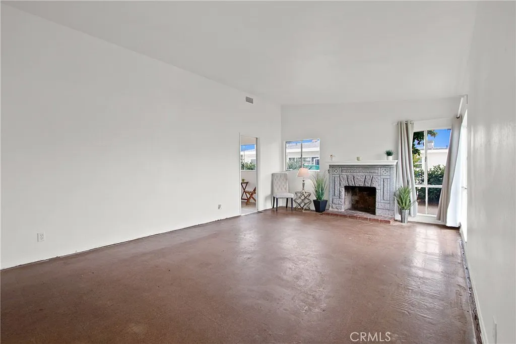 Room with white walls, concrete floor, fireplace, large windows, and a chair.