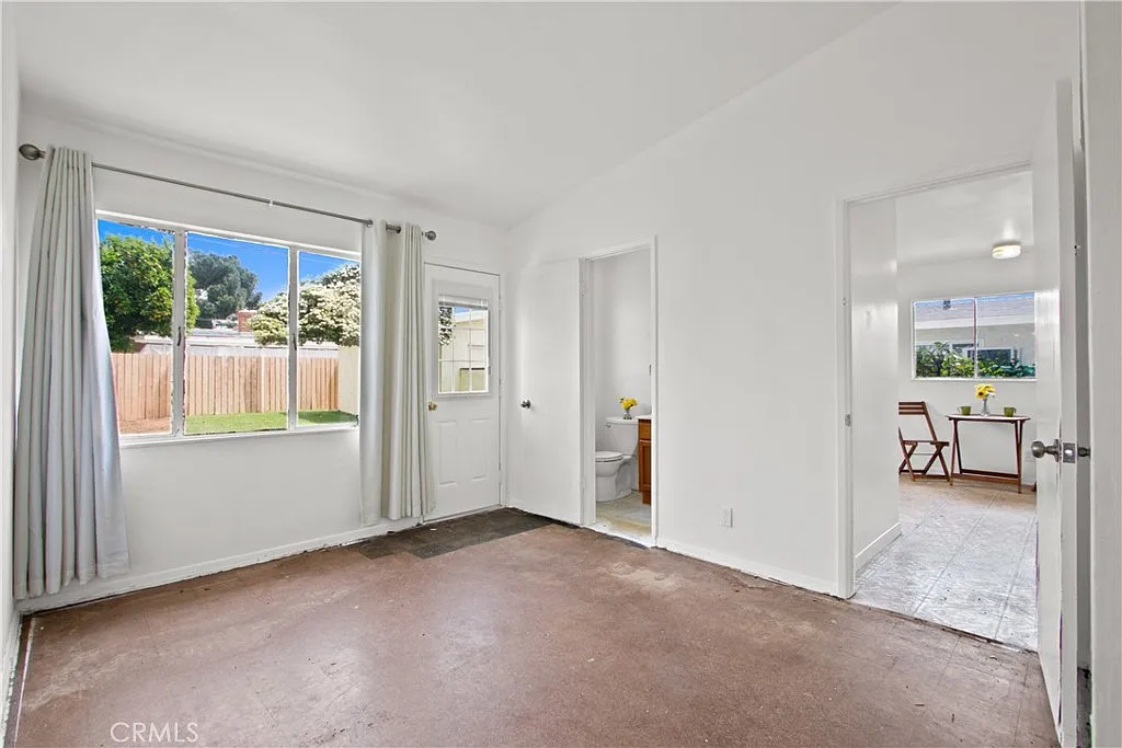 Empty room with white walls, a window, a door outside, and a partially visible door to a bathroom.