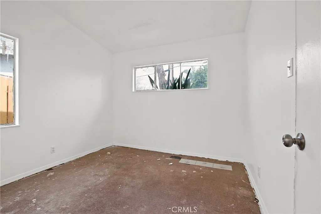 Empty room with white walls, a window, a door, and a bare brown floor.