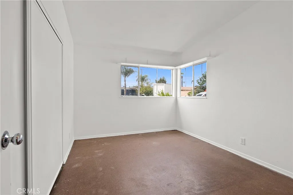 Empty room with white walls, a window, a door outside, and an open doorway to another room.