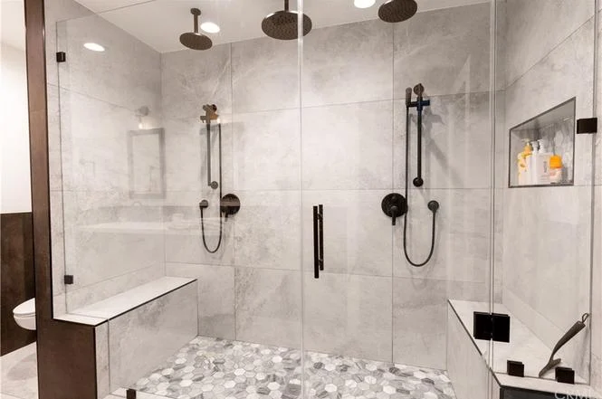 Modern bathroom with large glass shower, multiple shower heads, marble walls, and decorative floor