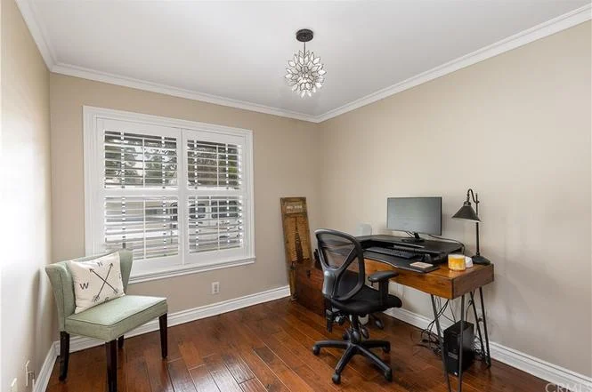 Home office with desk, computer, office chair, decorative light, small green chair, wooden floor, and window blinds letting in natural light