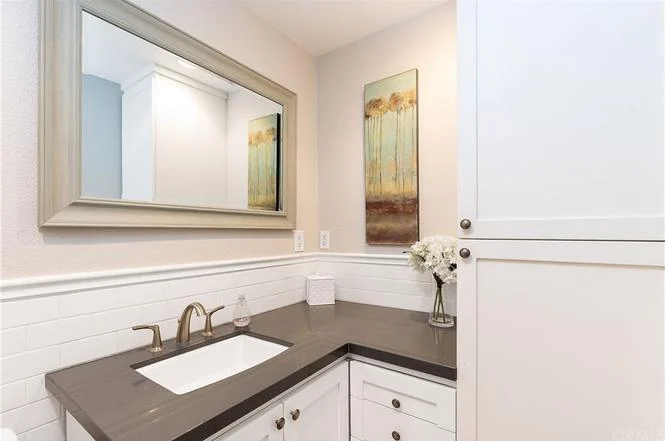 Bathroom with sink, dark countertop, white cabinets, large mirror, and decorative wall art