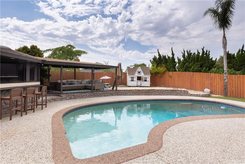 Backyard with swimming pool, stone edge, patio furniture, small shed, trees, and wooden fence