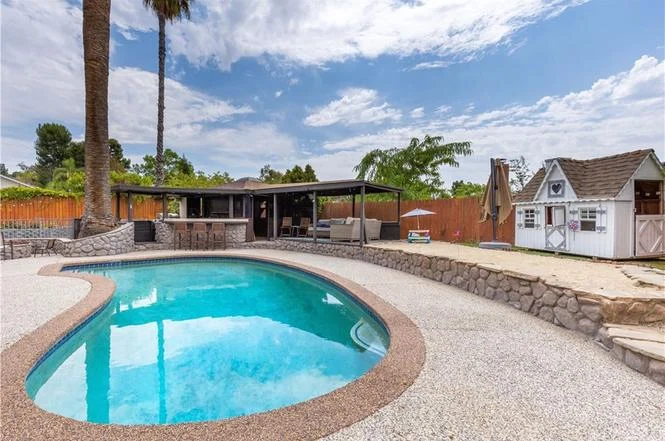 Backyard with swimming pool, stone patio, palm trees, and small playhouse