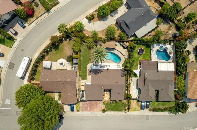Aerial view of suburban neighborhood with houses, swimming pools, and landscaped yards along curved street
