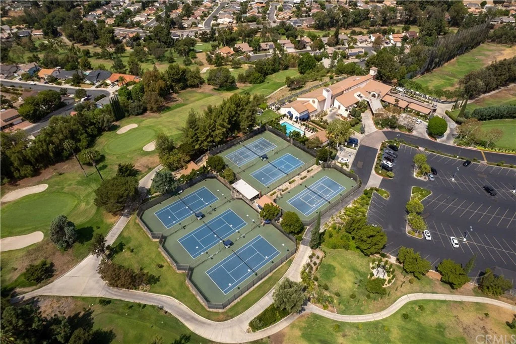 Aerial view of tennis complex with multiple courts, surrounded by greenery and houses