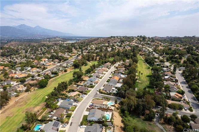 Aerial view of residential area with houses, green spaces, and mountains in background