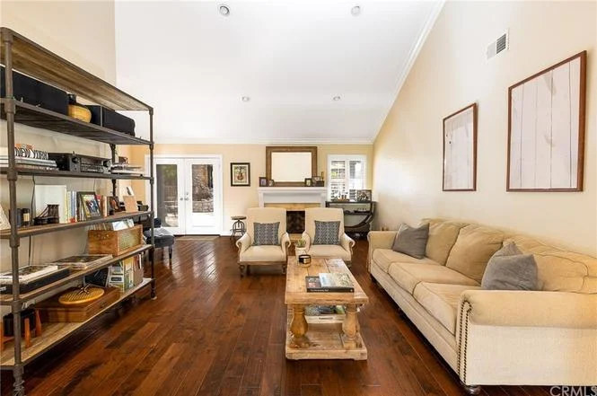 living room with hardwood floors, beige couch, rustic coffee table, large glass doors letting in light, and shelf with books and decor