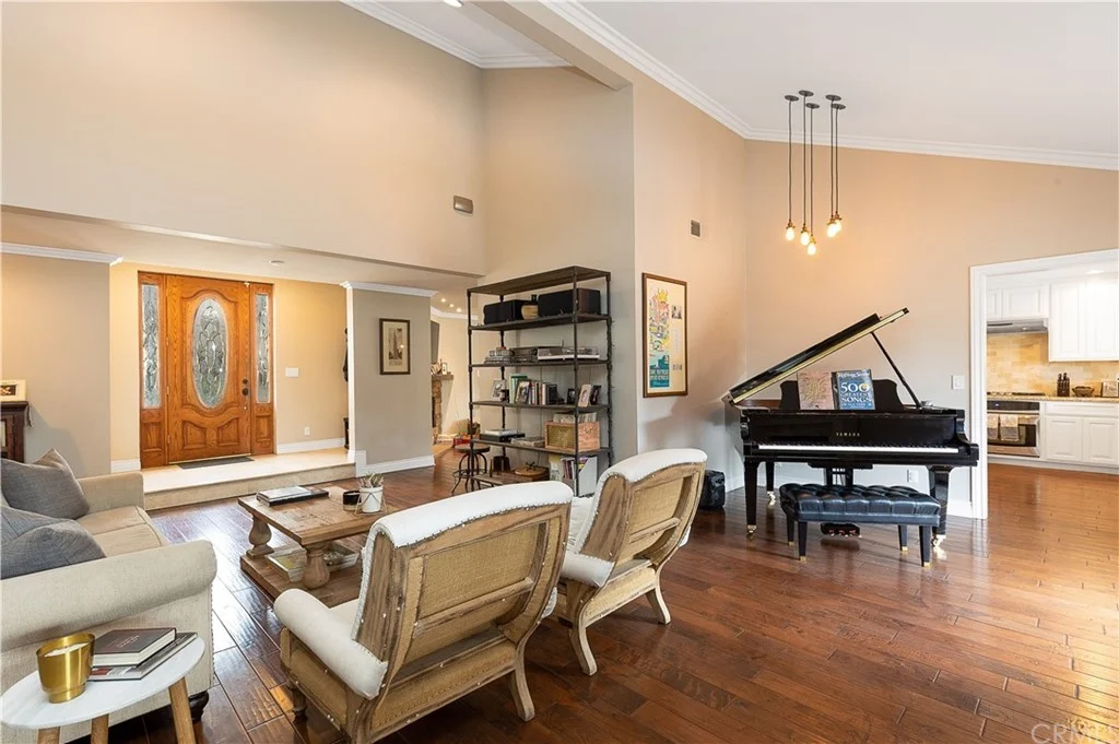 living room with wooden floors, grand piano, seating area, and entryway in background