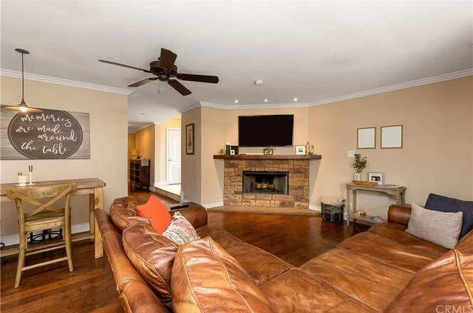 living room with stone fireplace, wall-mounted TV, leather sectional sofa, small dining table, light walls, and dark wood floor