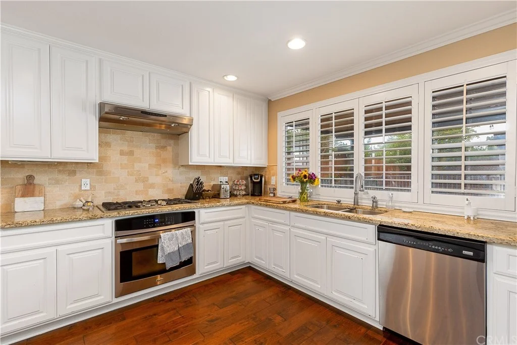 kitchen with white cabinets, stainless steel appliances, granite counter tops, and vase of flowers by window