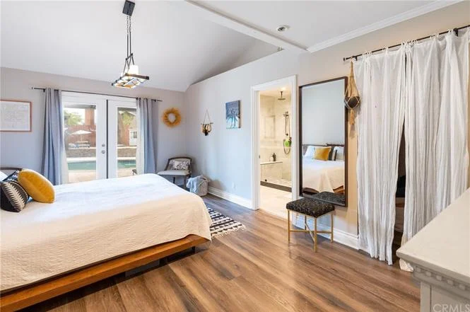 bedroom with large bed, white bedding, yellow pillow, hardwood floors, dresser, wall-mounted TV, and door to another room