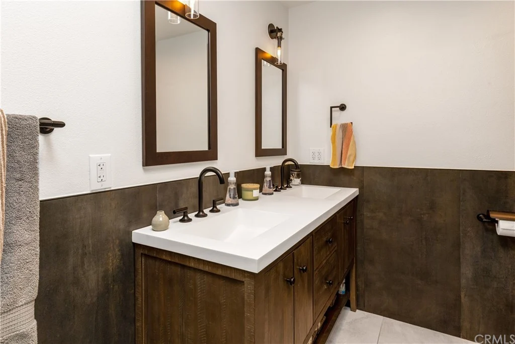 bathroom with double sink vanity, white countertop, dark wood cabinets, two mirrors, stylish fixtures, and towels on rack
