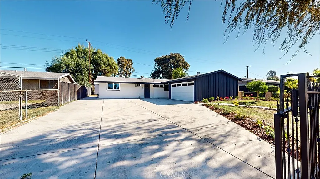 A single-story house with two garage doors, a large driveway, and greenery around it.