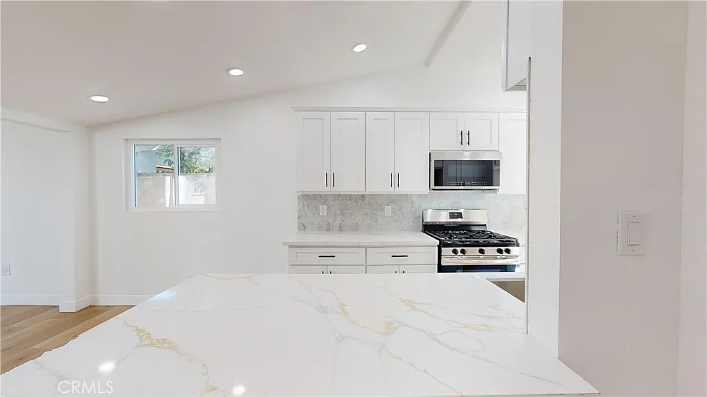 A kitchen with white cabinets, marble countertop, and stainless steel appliances.