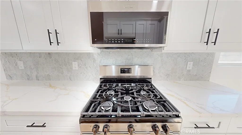 A kitchen stove with stainless steel hood and marble countertops.