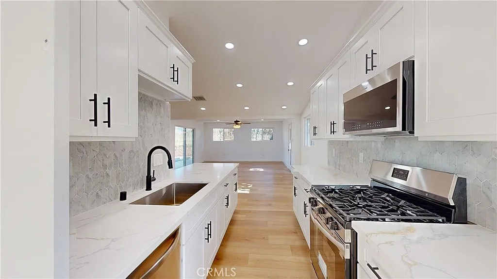 A kitchen with white cabinets, stainless steel stove, black faucet sink, and light marble countertops.