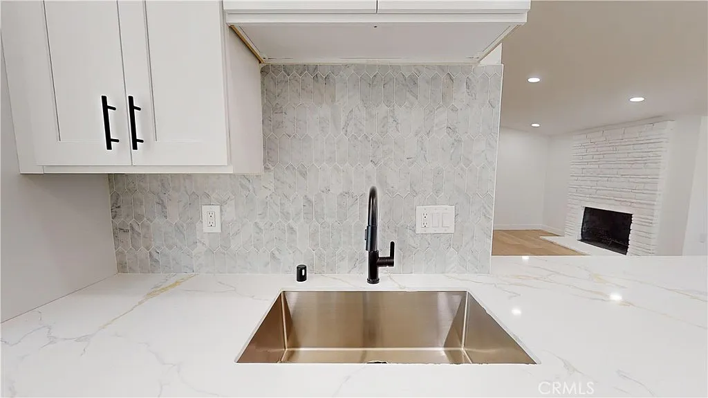Kitchen sink with black faucet, marble backsplash, and white cabinets.