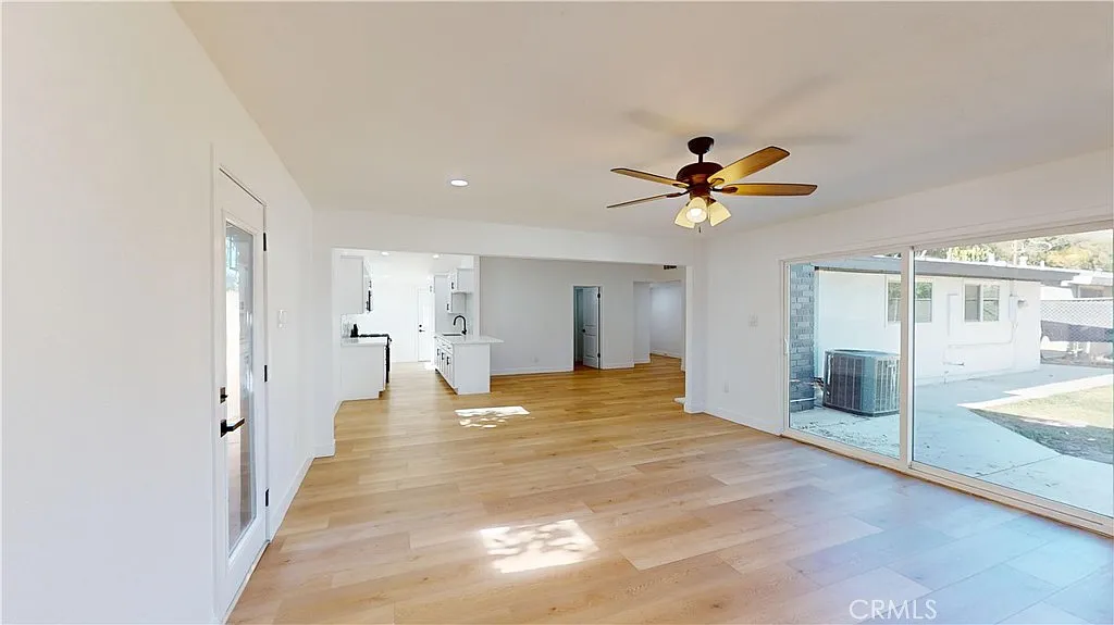 Living area with hardwood floors, ceiling fan, large windows, and access to outdoor space.
