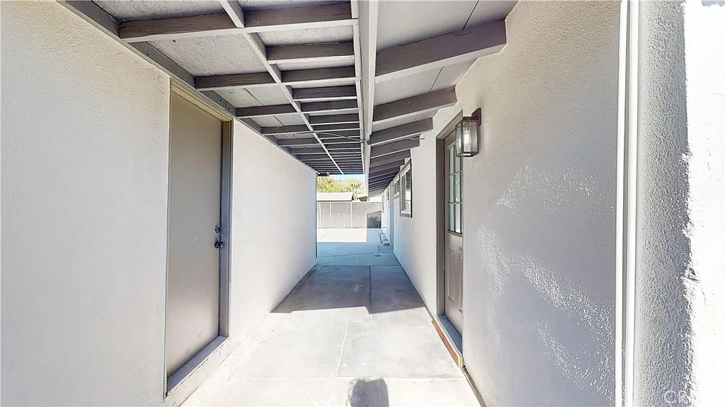 Narrow corridor between buildings with gray walls and slatted roof leading to open area.