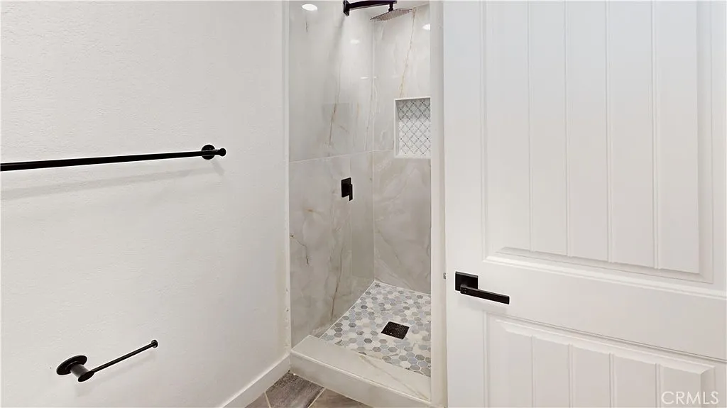 Shower with gray marble walls, mosaic tile floor, and black fixtures.