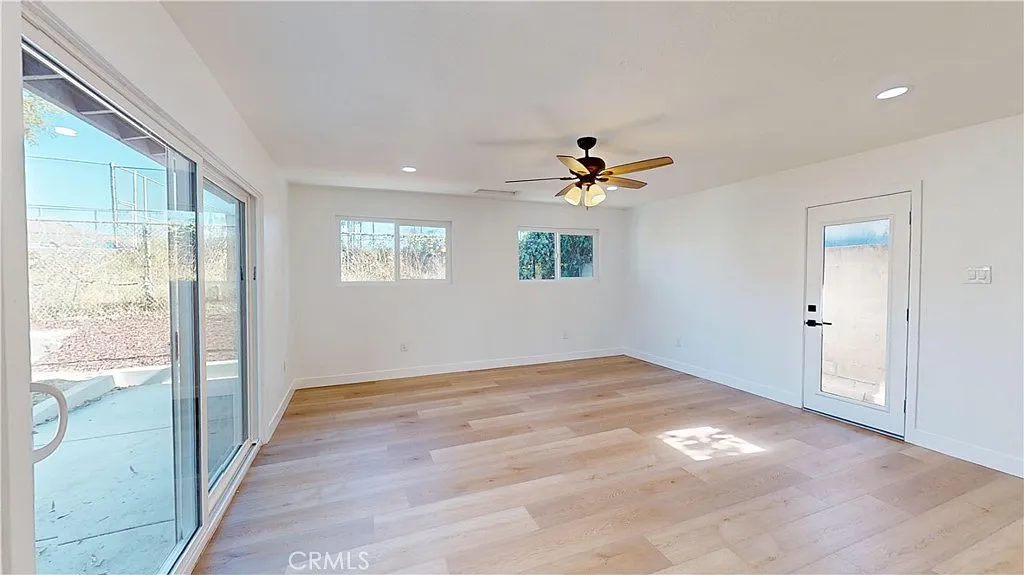Empty room with wooden floor, ceiling fan, large windows, and door to outside.