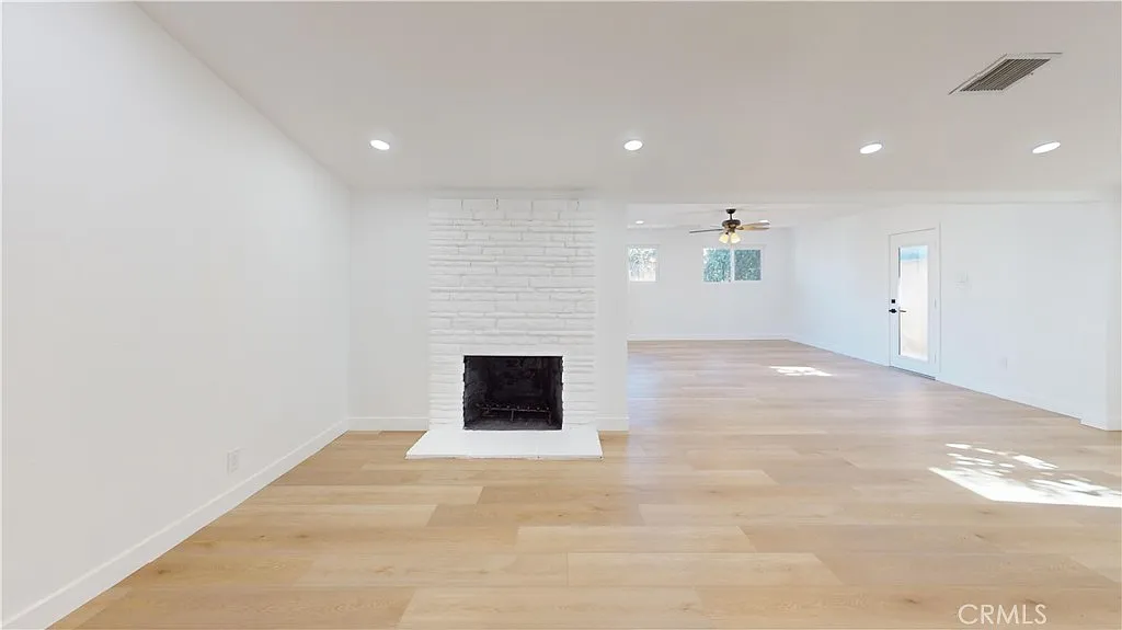 Empty living room with light wood floor, white brick fireplace, and recessed lighting.