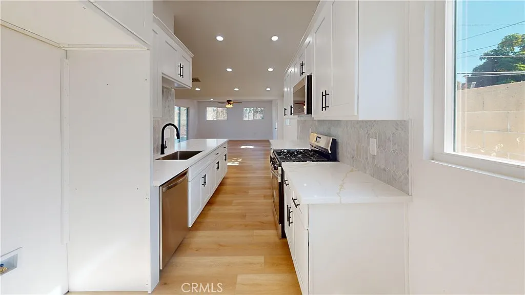 Kitchen with white cabinets, stainless appliances, large window, and light wood floor.