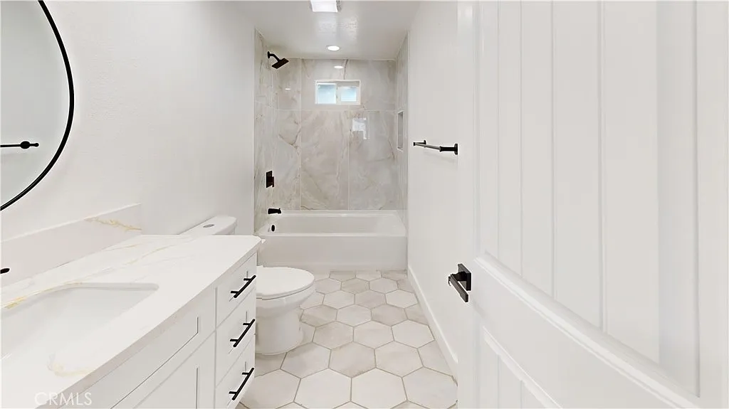 Bathroom with white walls, hexagonal tile floor, white bathtub, and round mirror above sink.