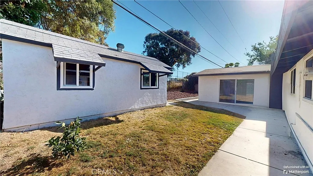 Backyard with two buildings, one with sloped roof and windows, another with glass sliding doors, and dry grass.