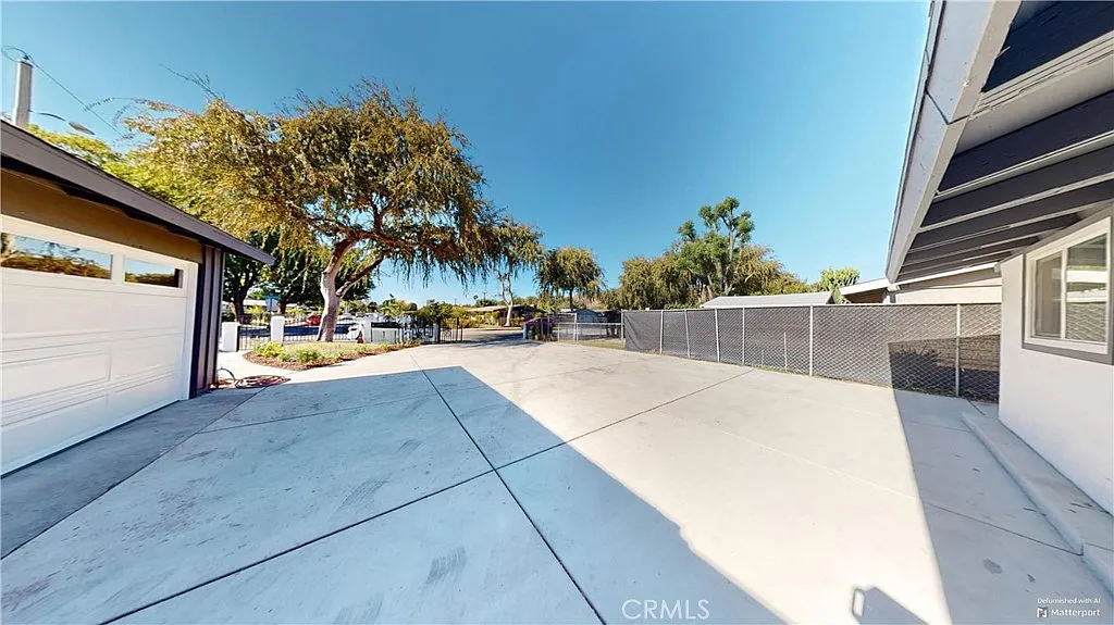 empty yard with concrete surface, trees, and fence.