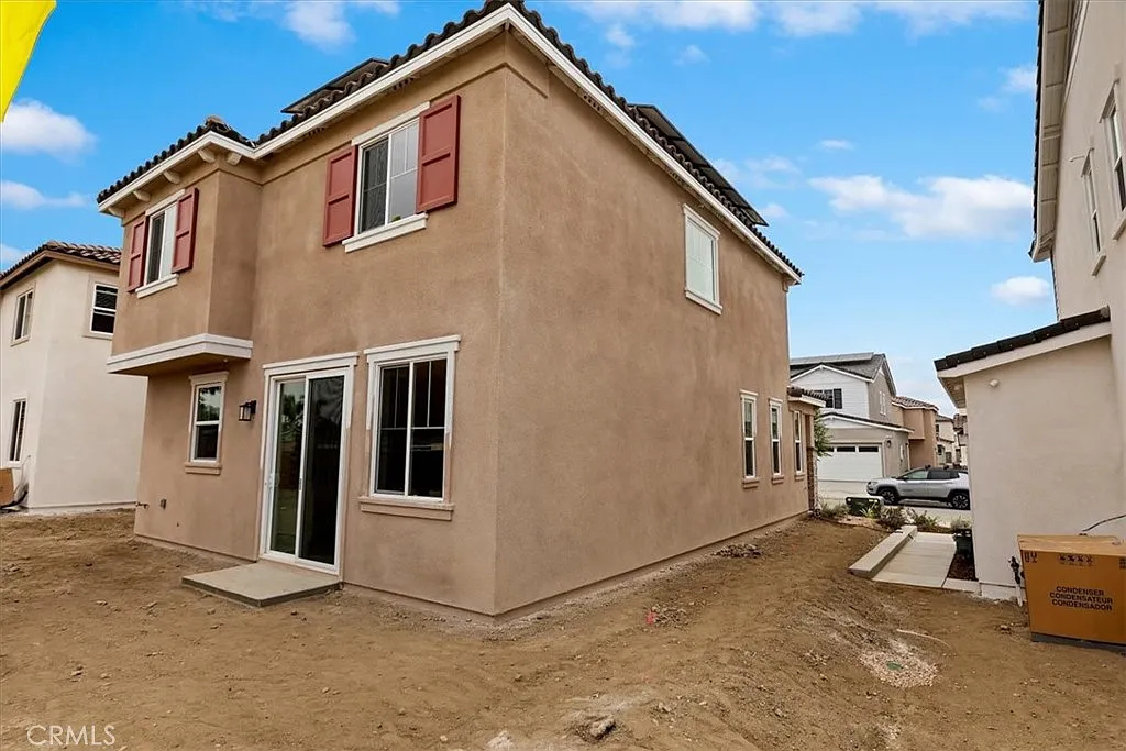 Two-story house under construction with stucco exterior, red shutters, and dirt lot.