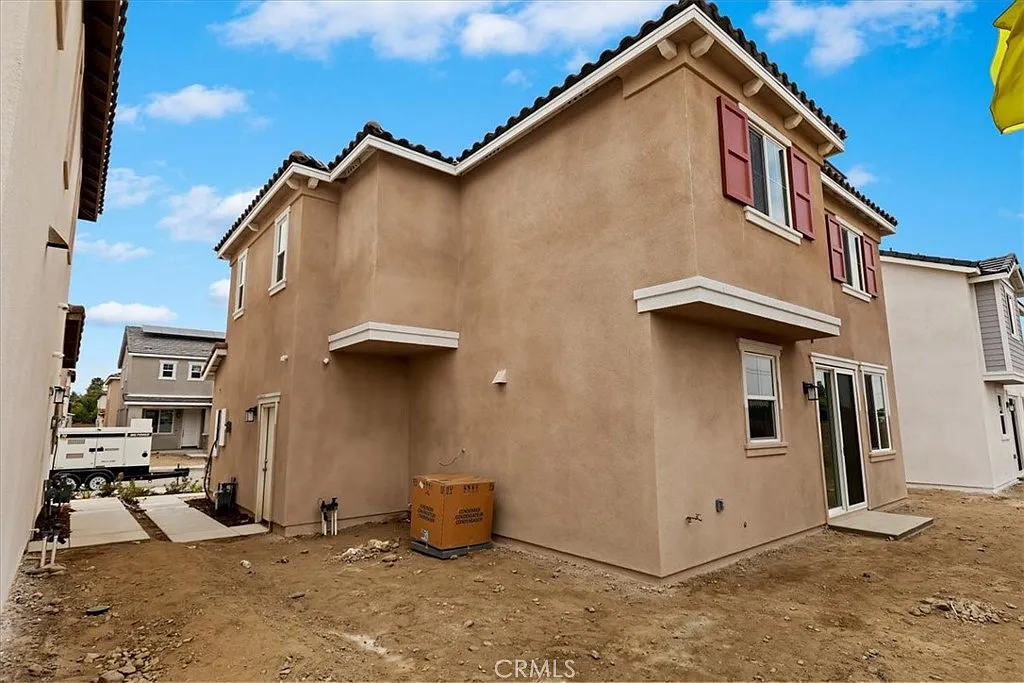 Two-story house with beige exterior, red shutters, and unfinished landscaping.