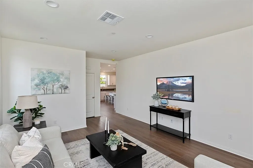 Living room with white couch, table with plant, TV, dark wood floor, and open space to kitchen or dining area.