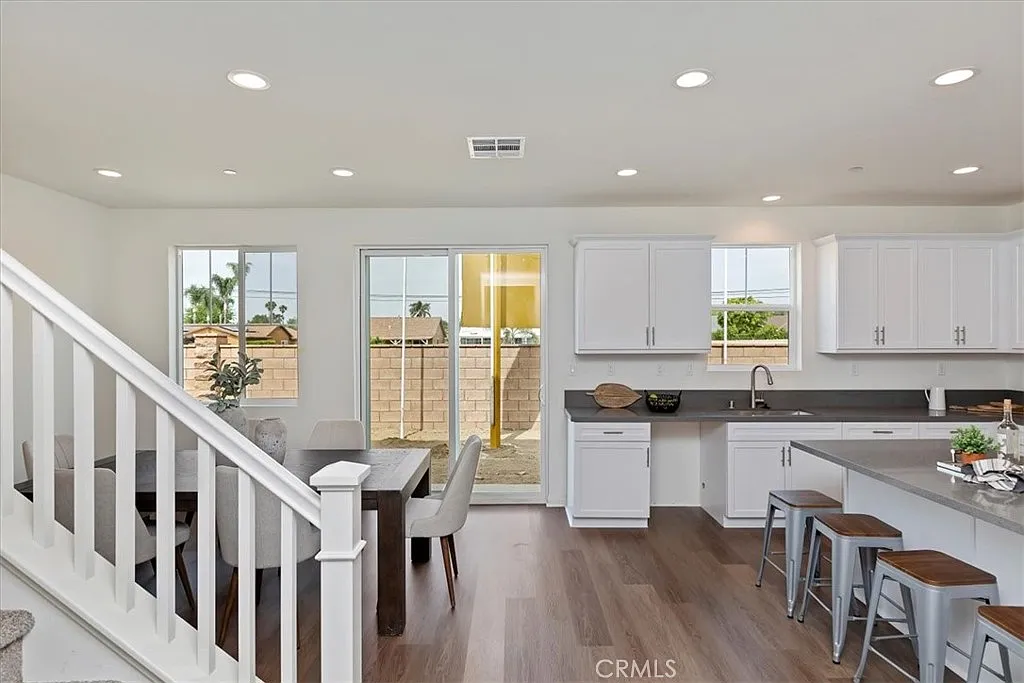 Kitchen with white cabinets, open layout, dining table, large windows, wooden floor, and patio door to outside.