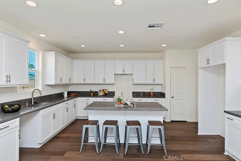 Kitchen with white cabinets, gray countertops, central island with three stools, and a window.
