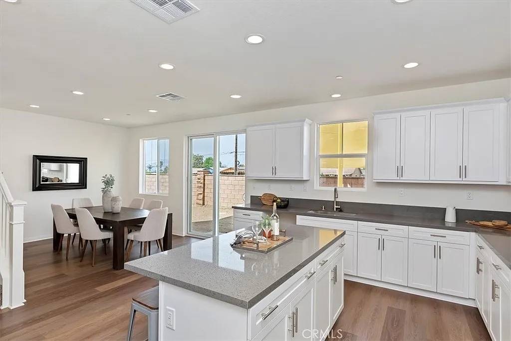 Kitchen with white cabinets, gray countertops, stainless appliances, wood floor, dining area, and sliding door to outside.
