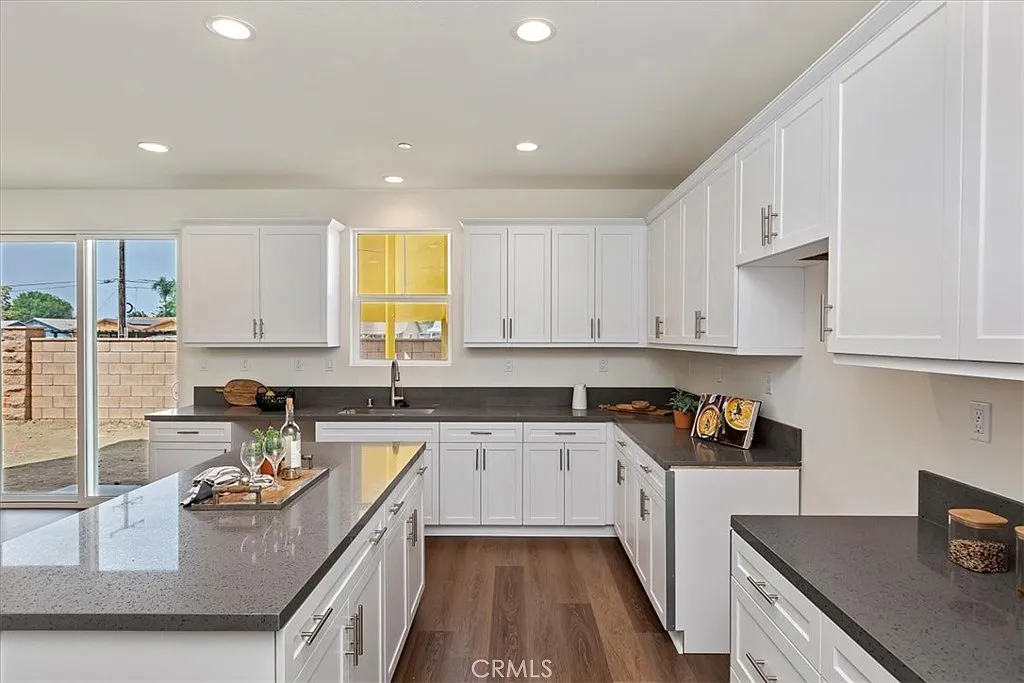 Kitchen with white cabinets, gray countertops, hardwood floor, and a window showing outdoor space.