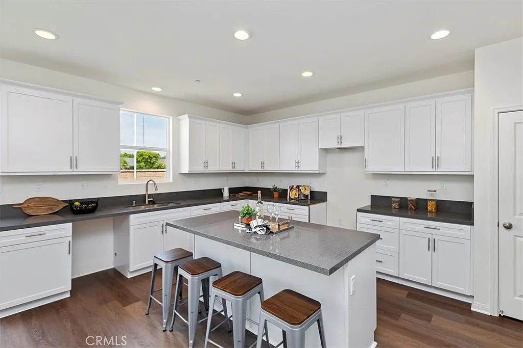 Kitchen with white cabinets, large gray island with seating, dark countertops, and a window.