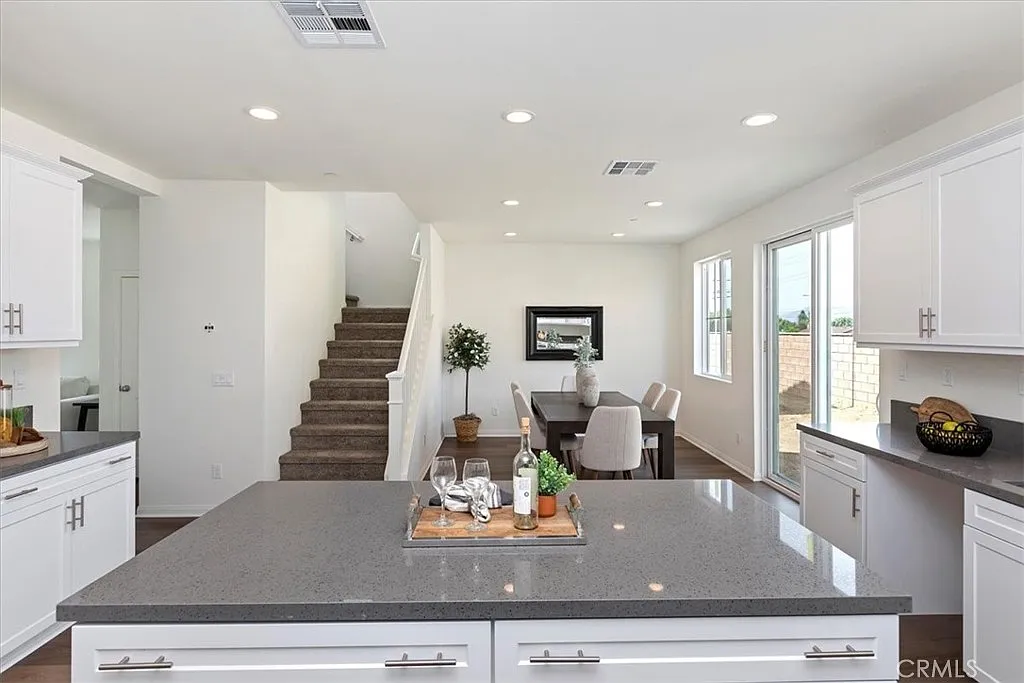 Kitchen with white cabinets, large island with dark countertop, and open layout to dining area and staircase.