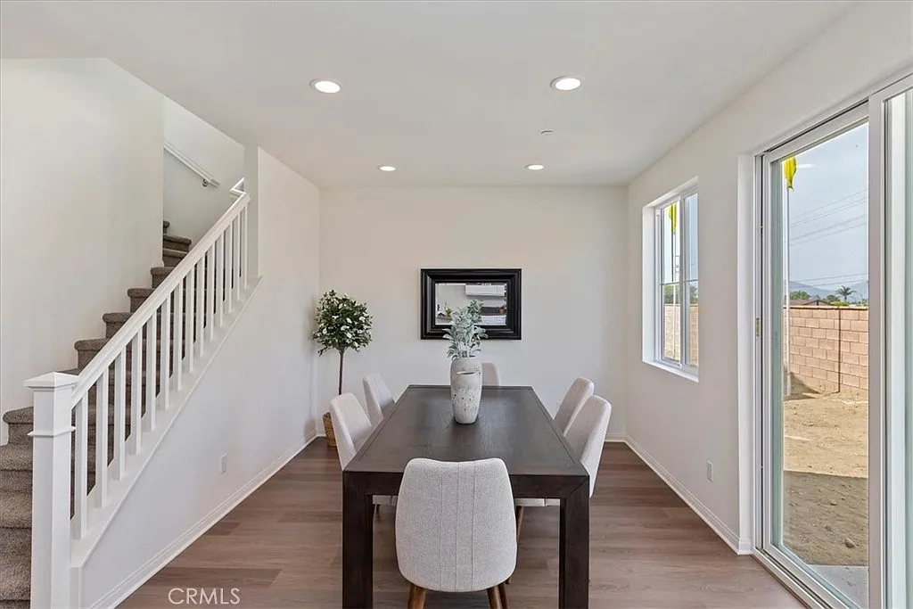 Dining area with large table, chairs, staircase, windows, plant, and wall art.