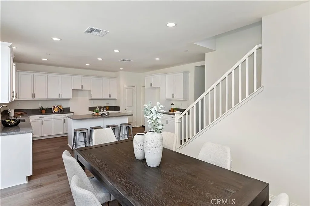 Kitchen and dining area with wooden table, white cabinets, barstools, and staircase in background.