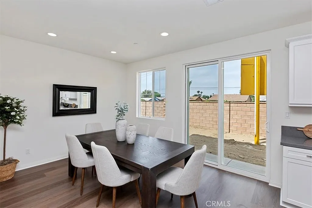Dining area with wooden table, white chairs, large windows, mirror, and a potted plant.