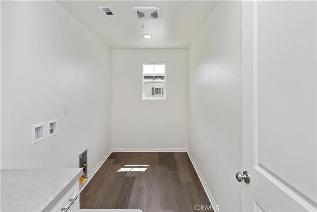 Empty laundry room with white walls, window, hardwood floor, and space for appliances.