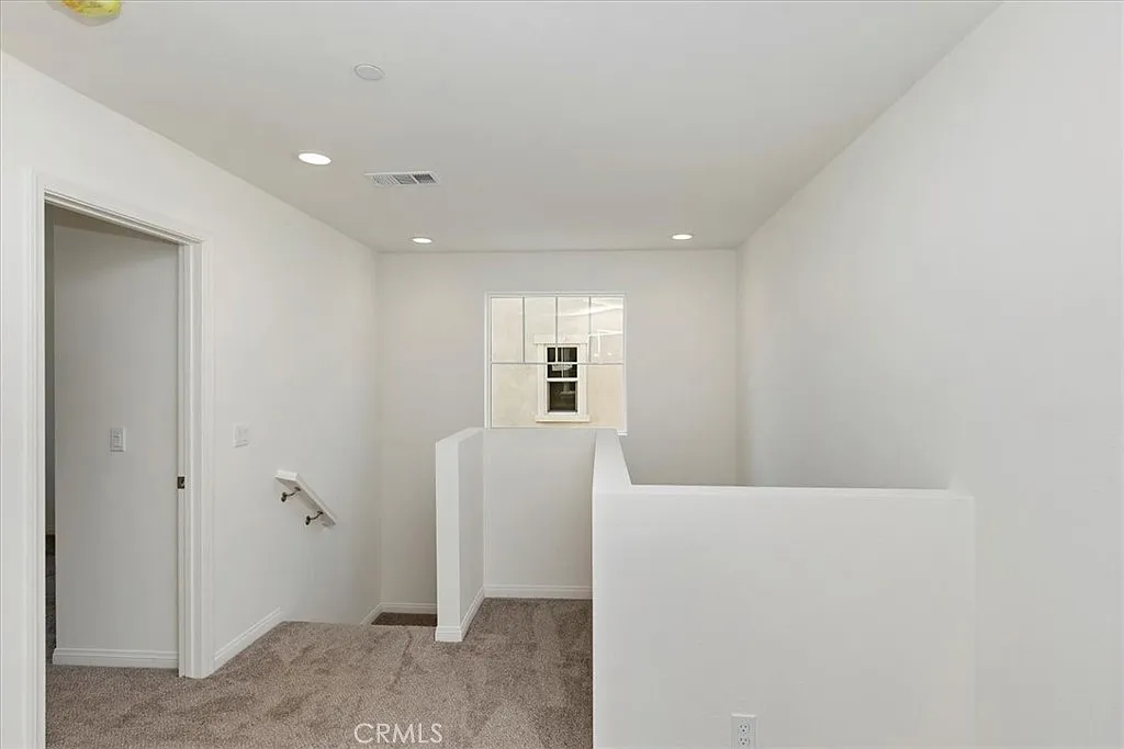 Light-colored hallway with carpet floor, white walls, and a window at the end.