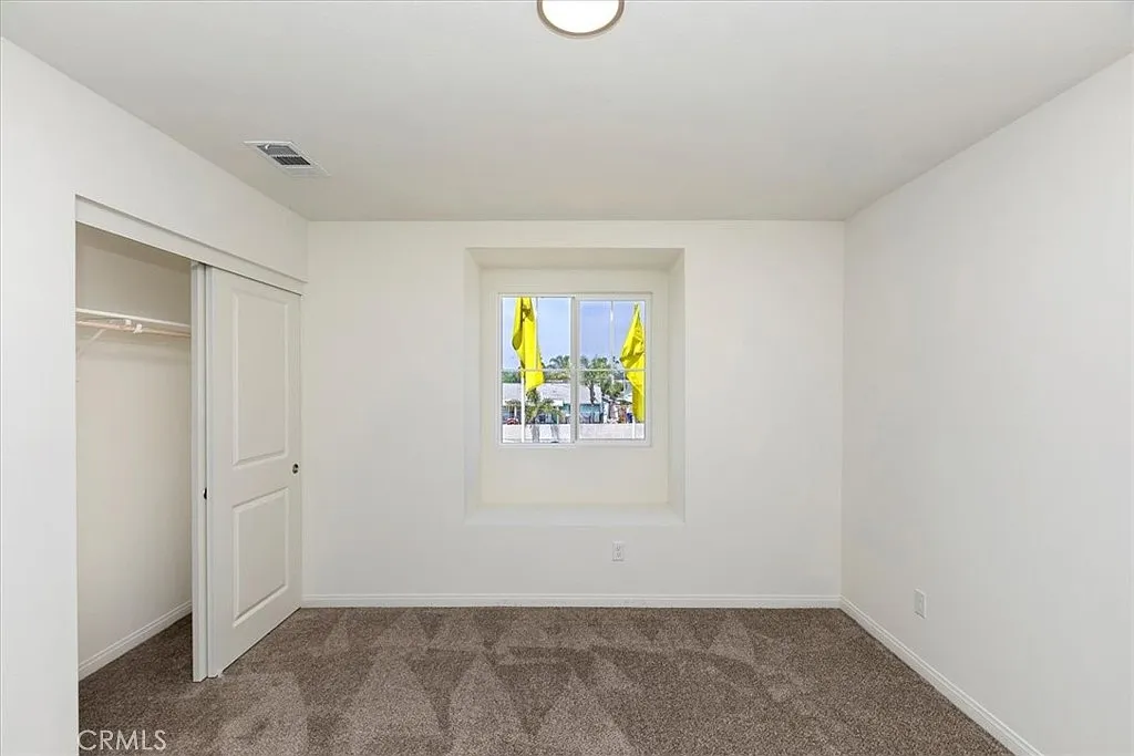 Empty room with light walls, carpet floor, a window with flags outside, and a closet.
