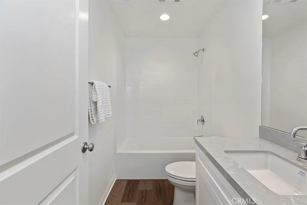 Bathroom with white bathtub, shower, toilet, and sink with light countertop.