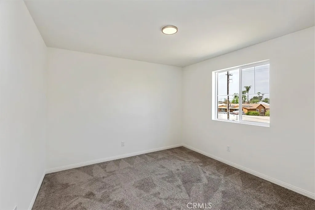 Empty room with white walls, carpet floor, and a window showing outside.